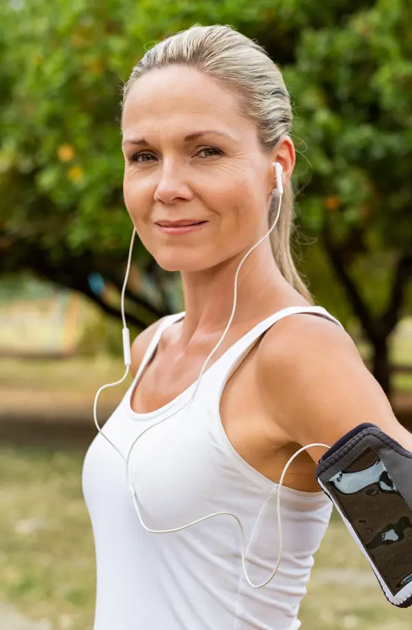 A fit middle aged woman wearing earphones and a tank top smiles after a run. Get insulin resistance treatment from Raving Health in Virginia Beach.