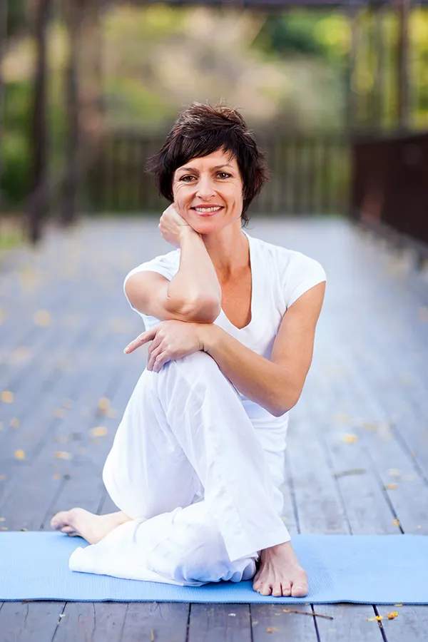 Osteoporosis-Treatment A middle-aged woman happily sits in a yoga pose. Get Osteoporosis treatment from Raving Health in Virginia Beach.