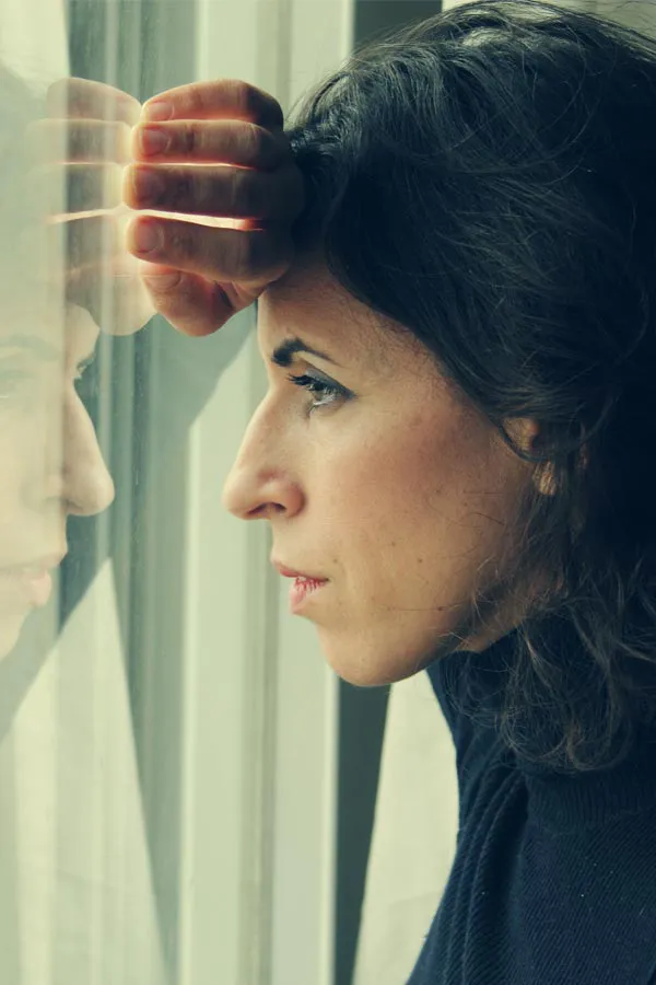 PCOS-Treatment A brunette woman in a thin dark turtleneck looks out the window with a serious expression, suffering from PCOS. Get treatment for Polycistic Ovarian Syndrome/PCOS from Raving Health in Virginia Beach.