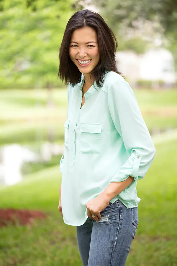 Perimenopause-Treatment A middle-aged brunette woman in a light green button-up shirt stands outside smiling, happy with her perimenopause treatment from Raving Health in Virginia Beach.