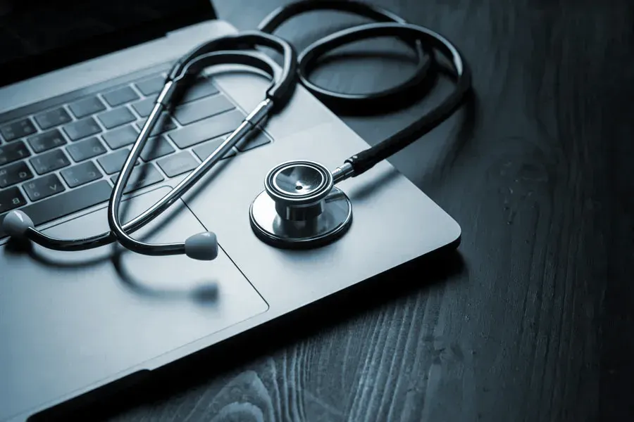 Telemedicine-Doctor An open laptop with a stethoscope lying on it on a wooden table, symbolizing telemedicine care from Raving Health in Virginia Beach.