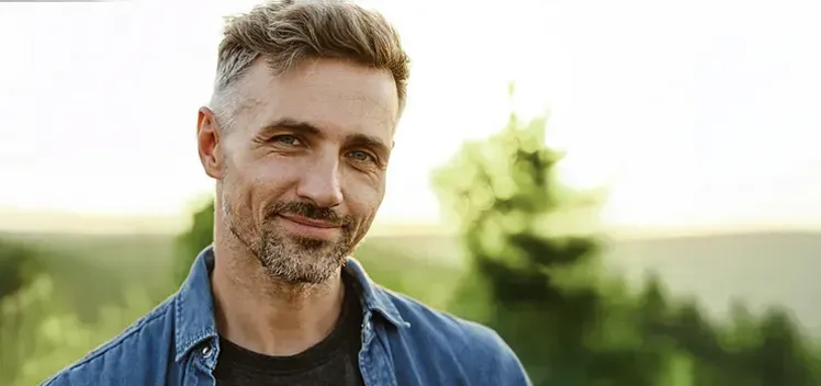 A middle-aged man smiling at the camera, feeling satisfied with Testosterone Replacement Therapy from Raving Health in Virginia Beach.